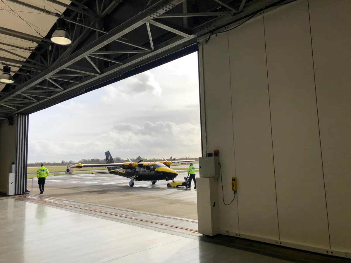 Guidage au sol affleurant d’une porte pliante de hangar, courant du piédroit jusqu’à l’aire de stationnement