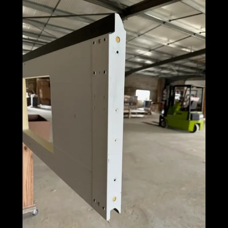 Détail de la tranche d’un panneau sandwich de porte sectionnelle : embout acier, perçages de patte à galet et découpe de hublot