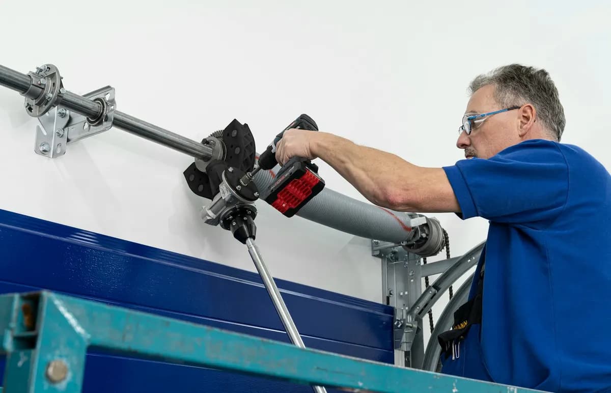 Technicien tendant l’arbre à ressorts de torsion d’une porte sectionnelle, avec paliers, rail latéral et entraînement à chaîne visibles