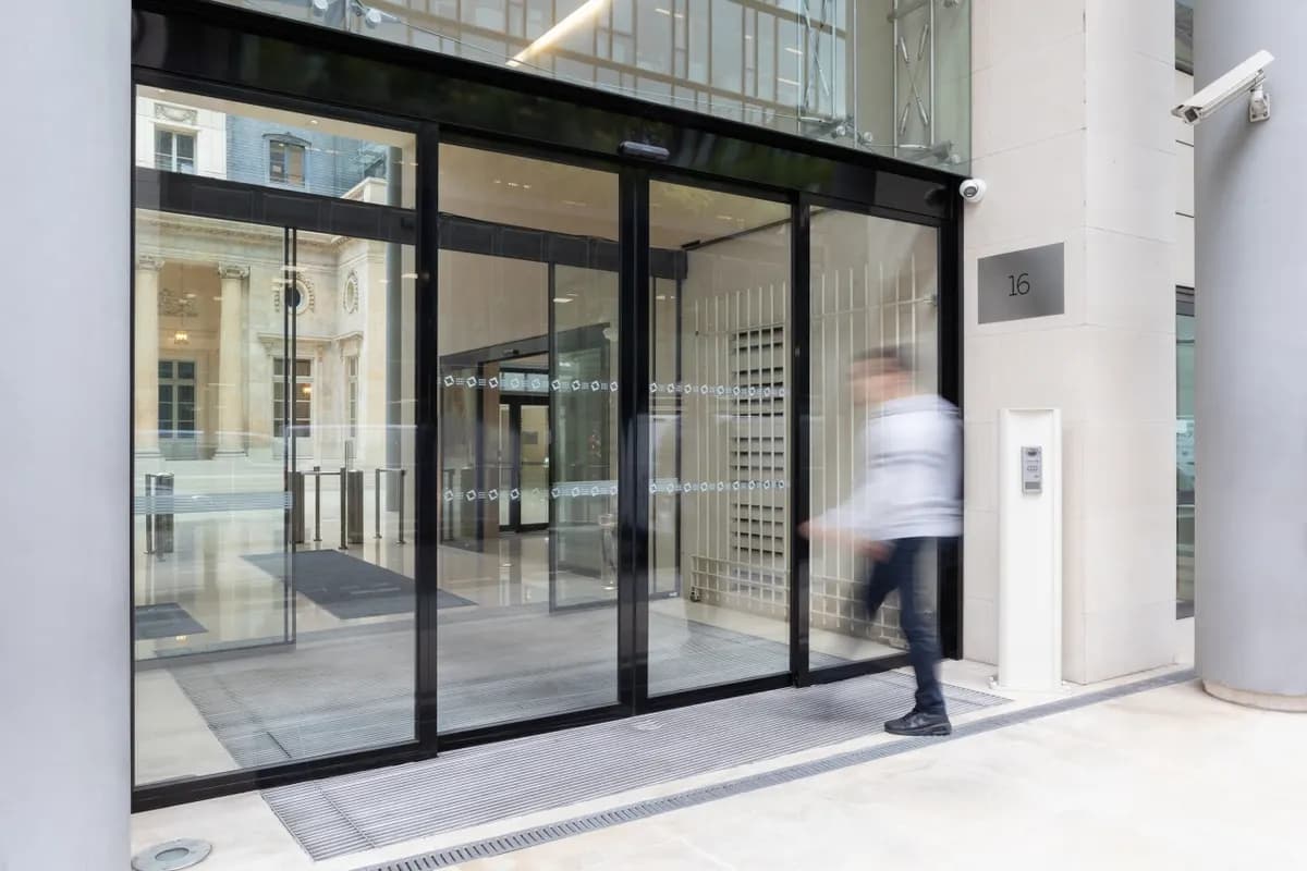 Porte automatique coulissante à châssis aluminium laqué noir et vitrage toute hauteur, à l’entrée d’un immeuble de bureaux