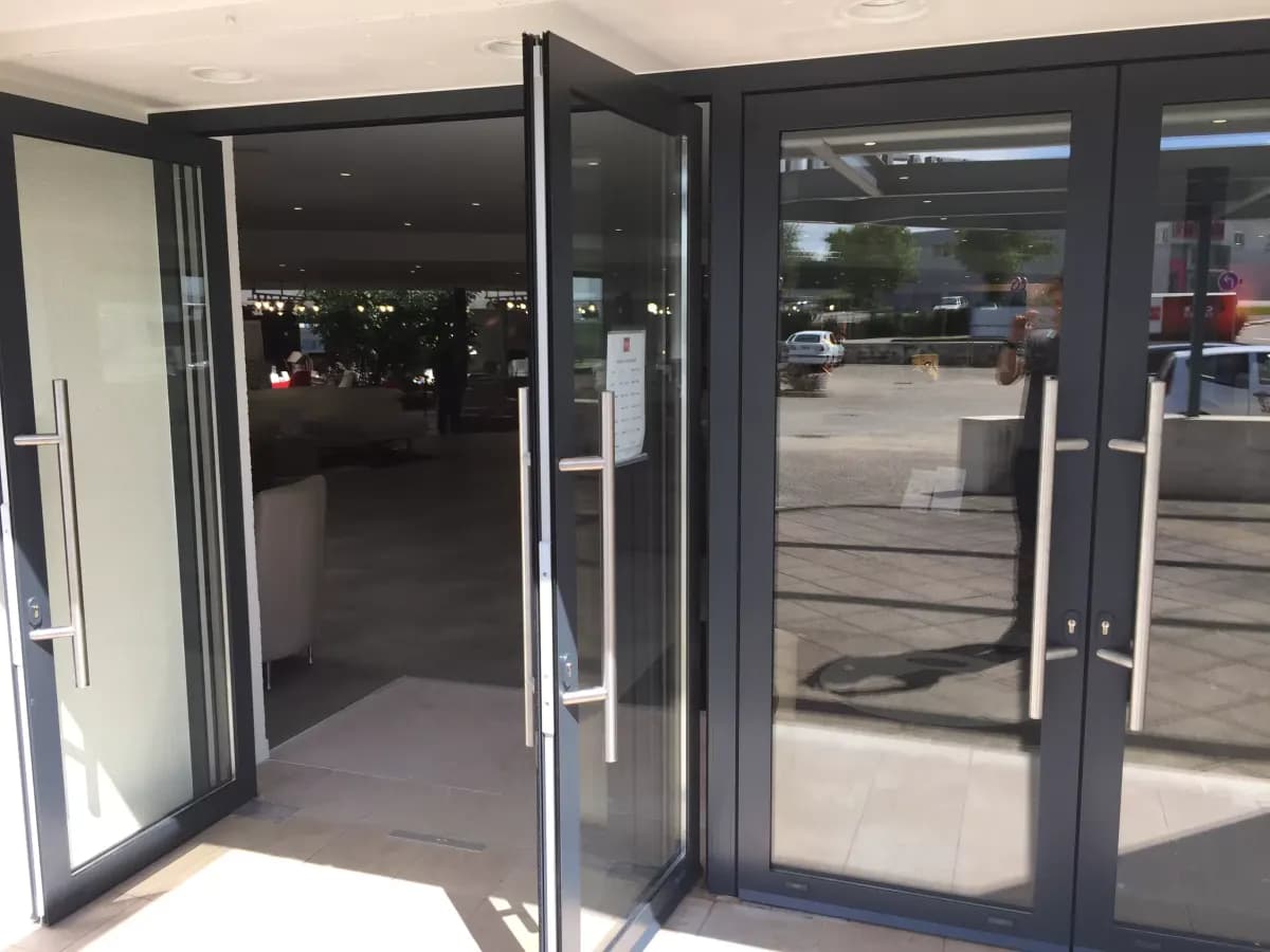 Poignées barre en inox et rosaces de serrure à cylindre sur des portes vitrées à châssis aluminium anthracite RAL 7016