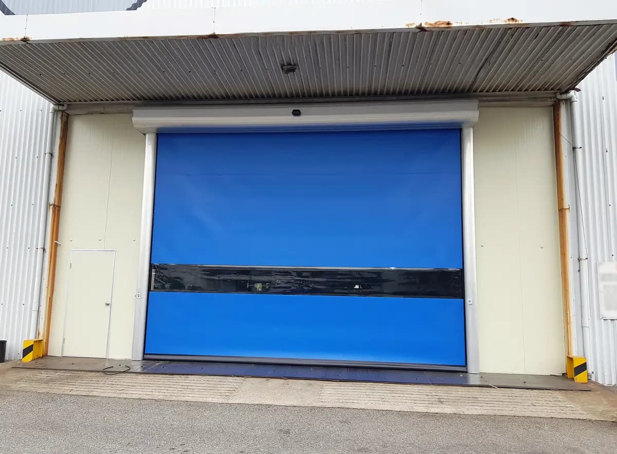 Portail rapide à toile PVC bleue entièrement déroulée sur une baie d’entrepôt, colonnes de guidage aluminium et enrouleur en tête