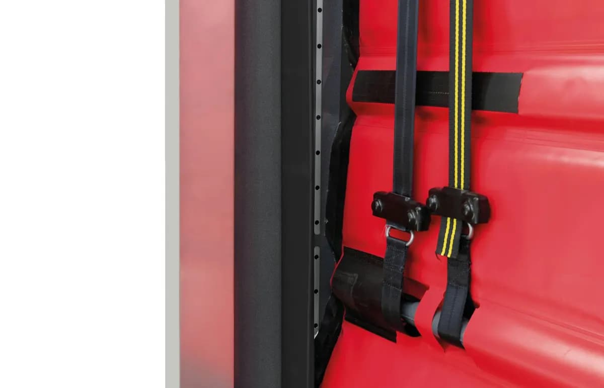 Détail de la colonne de guidage d’un portail rapide : profilé aluminium, bord de toile PVC et clips de réarmement après choc