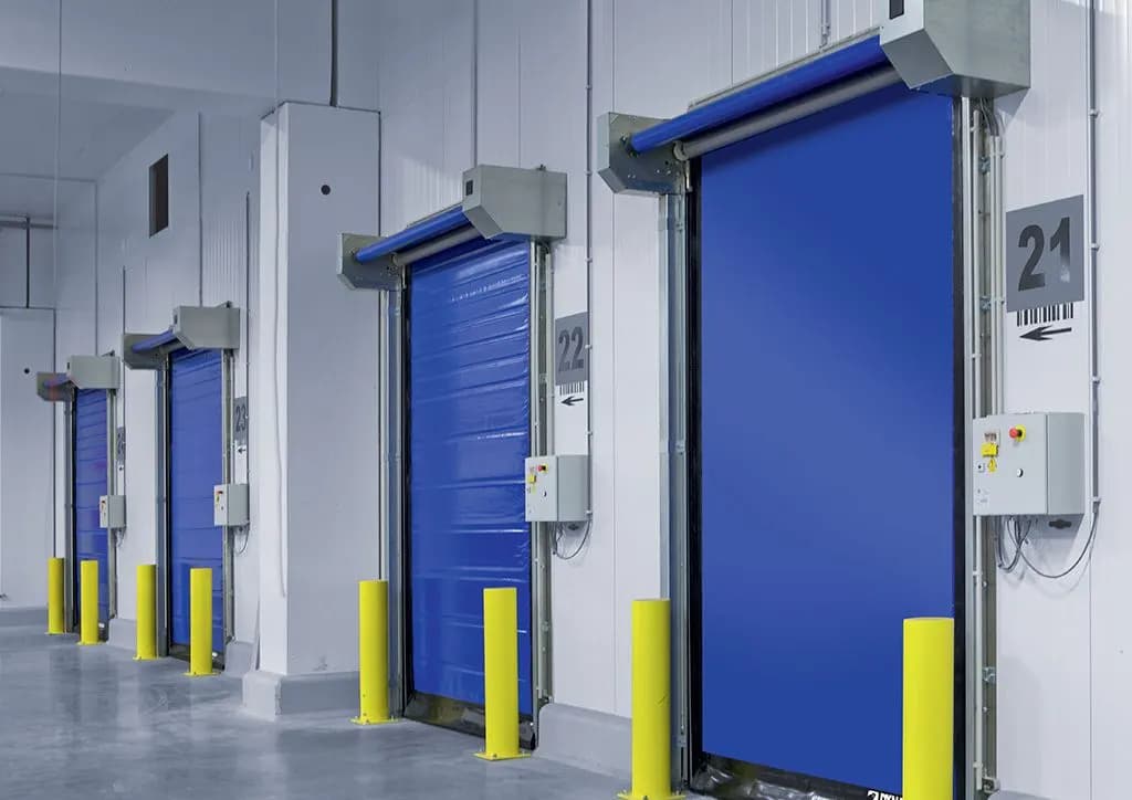 Variante chambre froide : quatre portails rapides isolés à toile PVC alignés sur une paroi en panneaux sandwich, avec chasse-roues