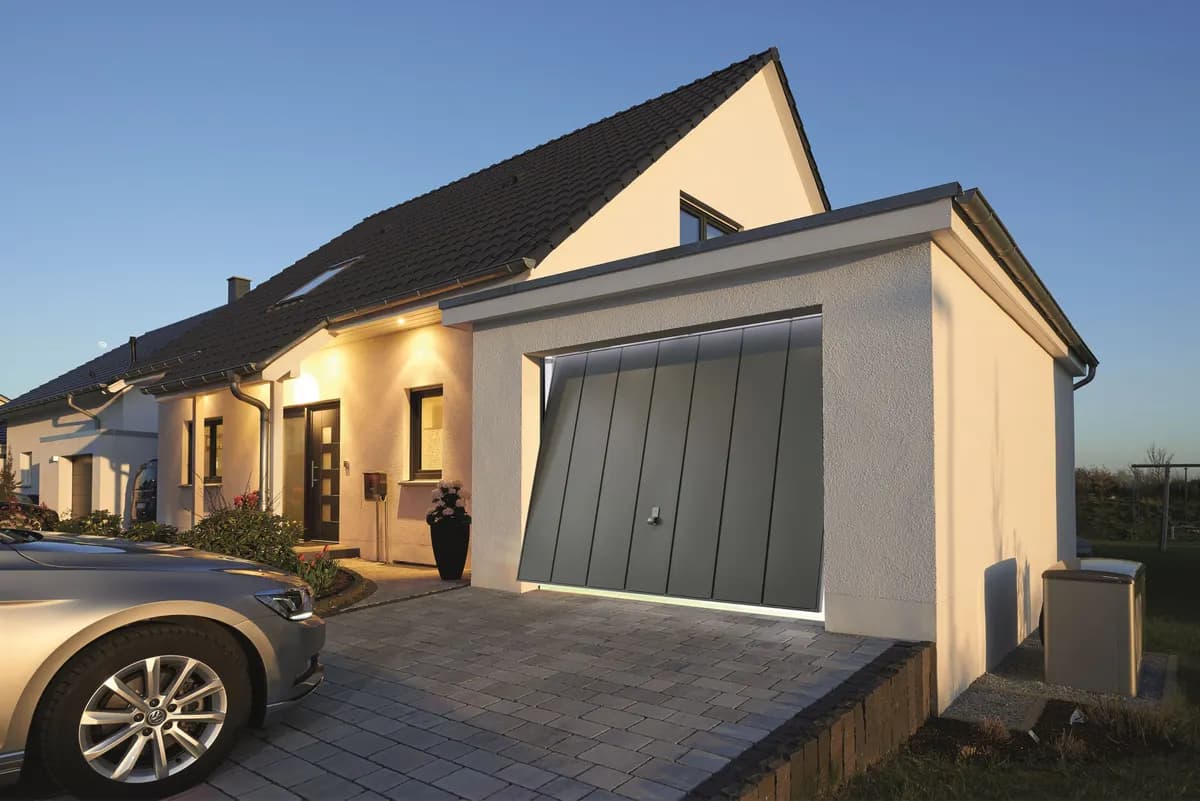 Porte basculante de garage à panneau monobloc nervuré, fermée en façade d’une villa avec allée pavée