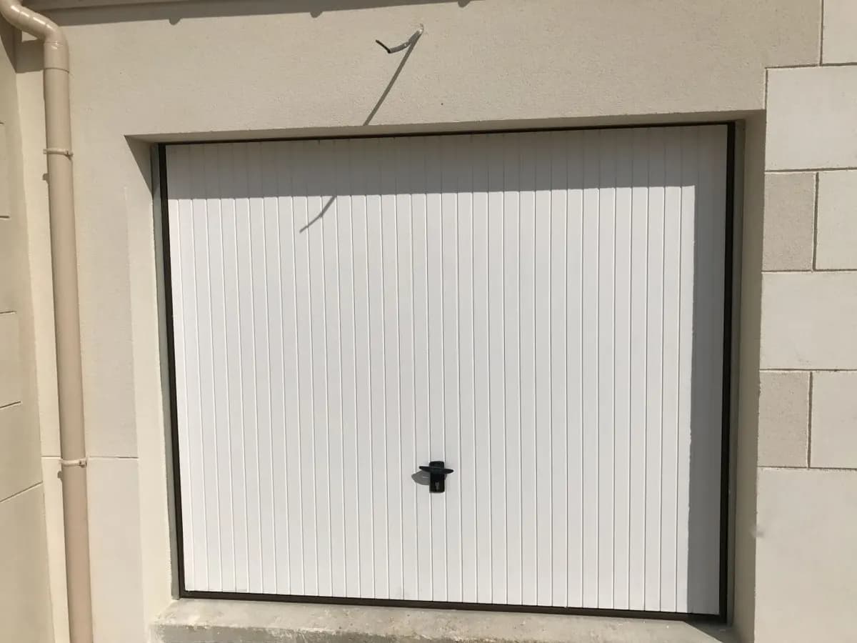 Détail frontal du panneau acier d’une porte basculante montrant la nervure verticale fine et la poignée-serrure centrale