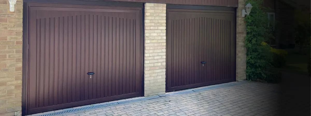 Variante finition bois : deux portes basculantes à nervures verticales et finition ton bois foncé, sur une maison en brique