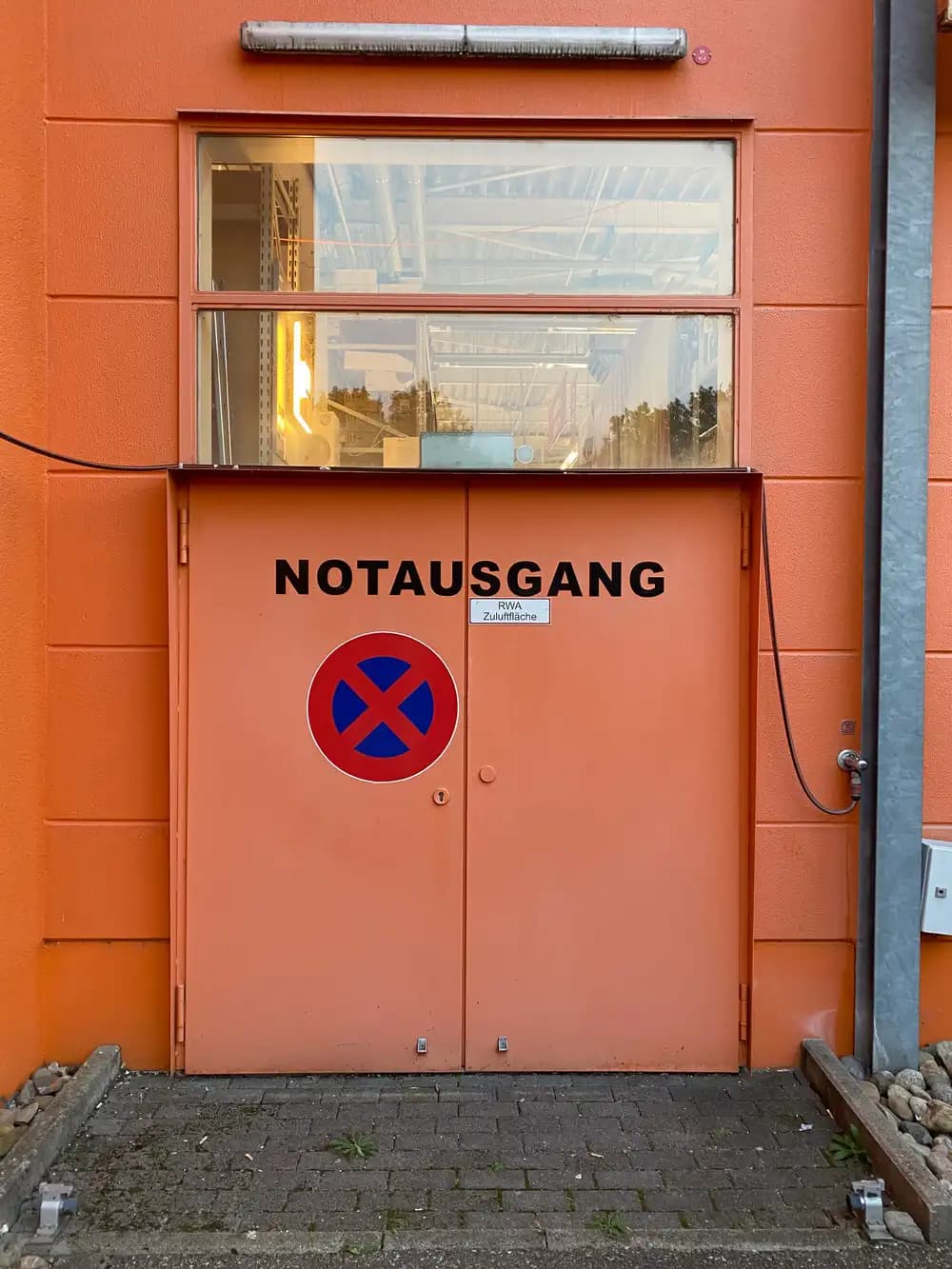 Porte battante métallique à un vantail ouverte dans une façade bardée, avec bâti acier et seuil, signalée comme issue de secours