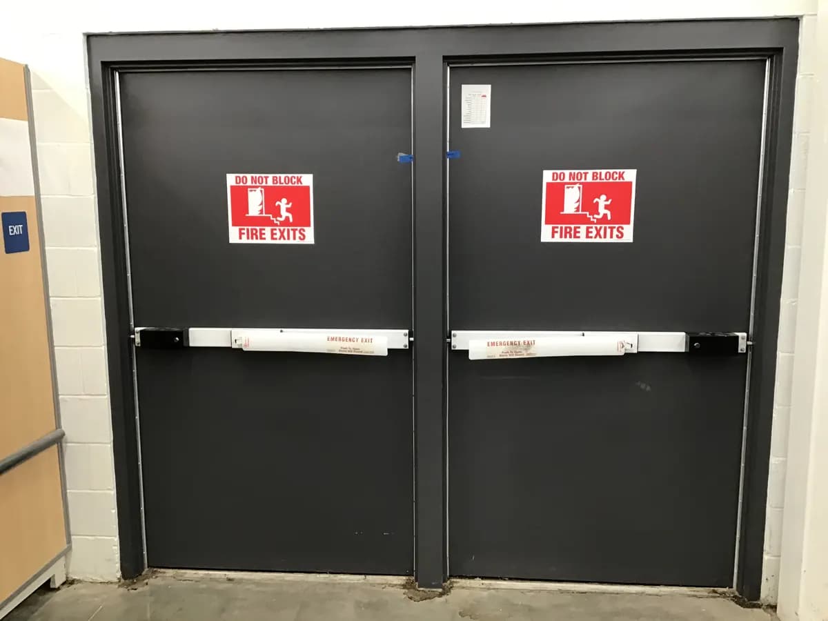 Deux portes battantes acier à barres anti-panique dans un couloir technique à murs en blocs béton
