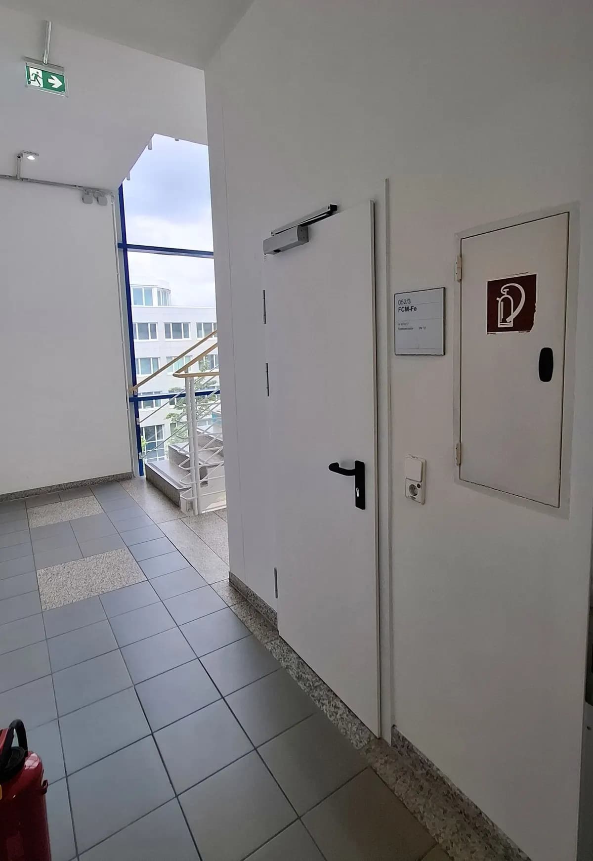 Porte coupe-feu métallique blanche à un vantail installée sur un palier d’escalier, avec ferme-porte en imposte et signalisation de secours