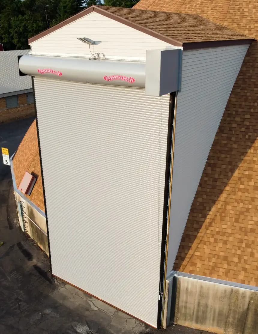 Caisson et tambour d’enroulement apparents en tête d’une porte enroulable industrielle, avec coulisse latérale et chaîne de secours