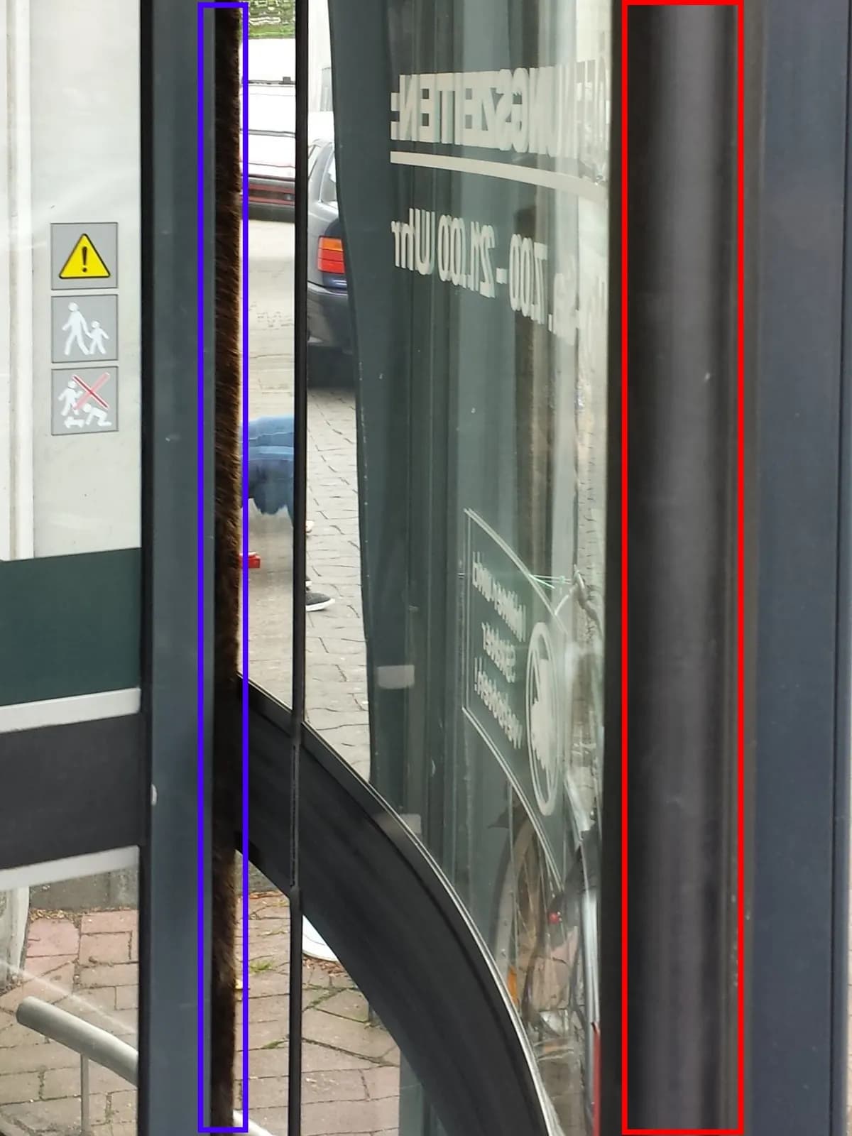 Barre palpeuse de sécurité rouge en bord de vantail de porte tambour, contre la paroi cylindrique vitrée