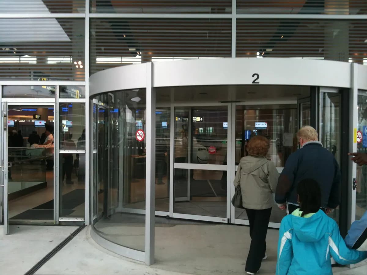 Porte tambour à canopée inox en service dans un hall d’aérogare, usagers franchissant le cylindre