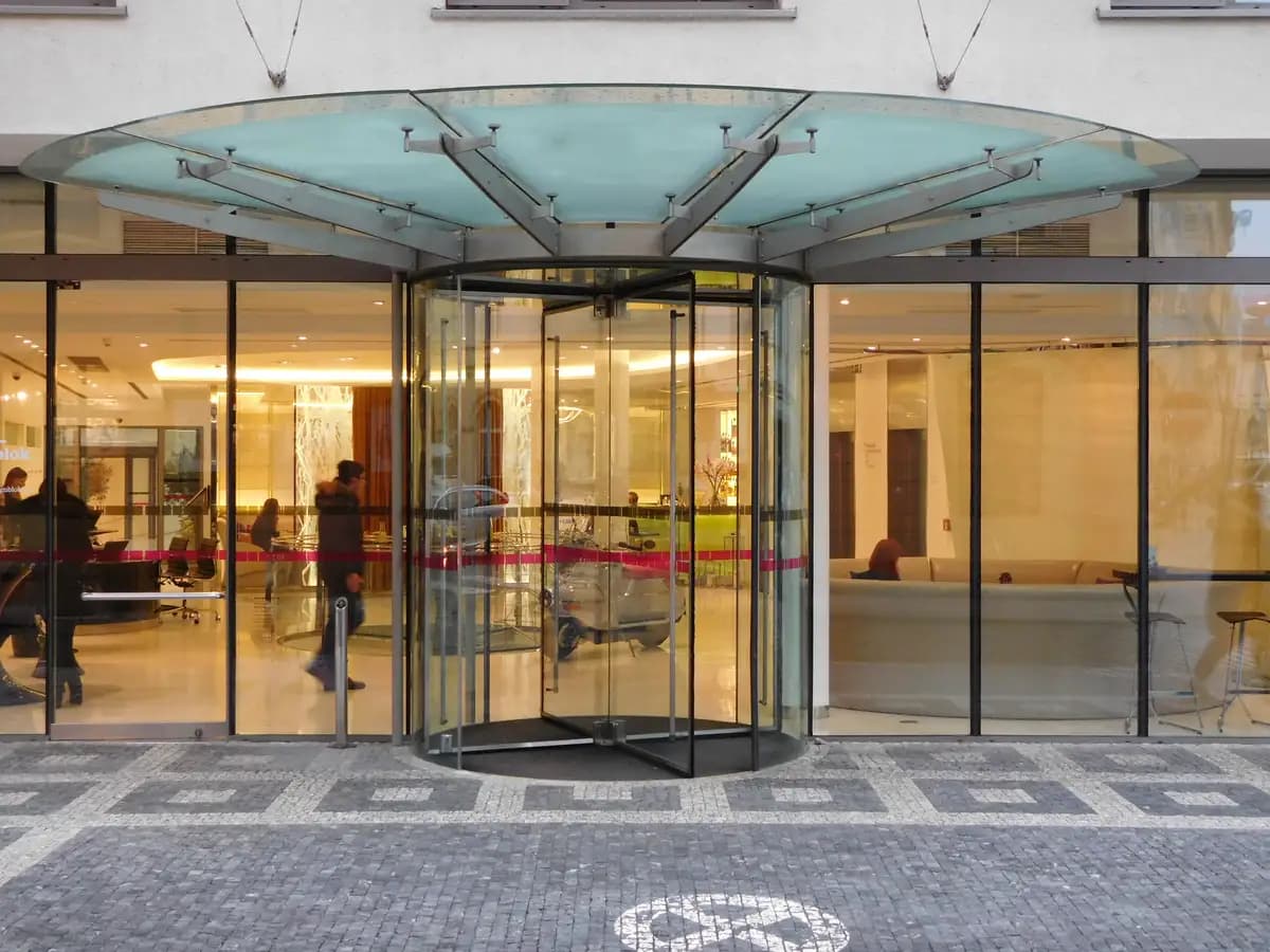 Porte tournante automatique toute vitrée à encadrement minimal, sous une canopée en verre à l’entrée d’un hôtel
