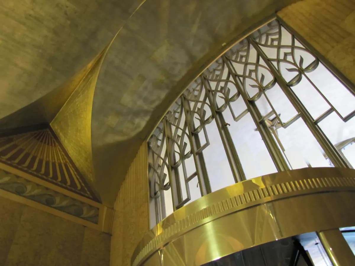 Couronne de canopée dorée et voûte technique au-dessus d’une porte tournante de hall d’immeuble