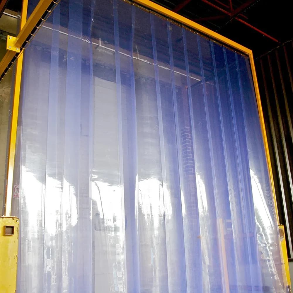Rideau à lanières PVC transparentes suspendu sur une large baie industrielle, protections de piédroit acier de part et d’autre