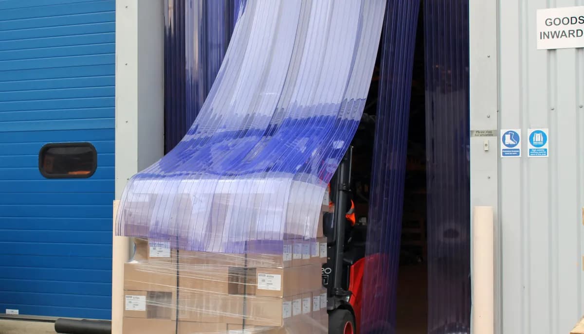 Chariot élévateur franchissant un rideau à lanières PVC avec une palette, les lanières s’écartant puis se refermant
