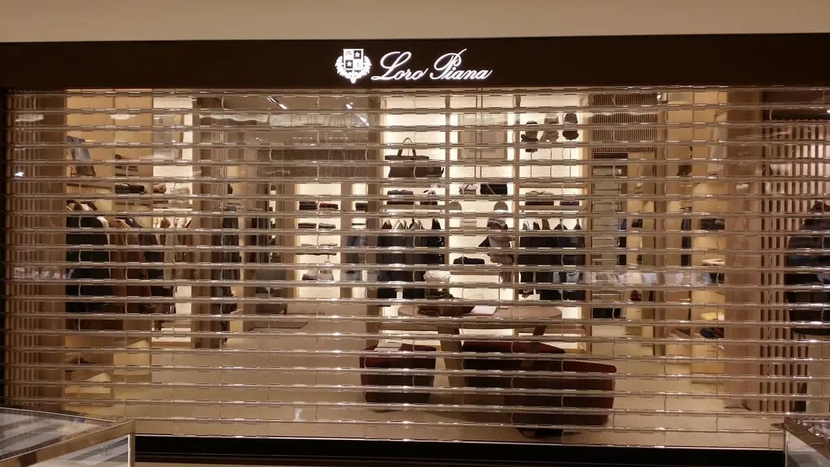 Boutique de galerie commerciale fermée derrière un rideau métallique à lames micro-perforées laissant voir la vitrine